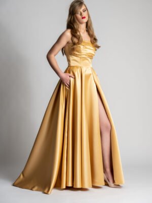 Elegant woman in a stunning gold debs dress with a high slit, posing confidently in a glamorous setting.